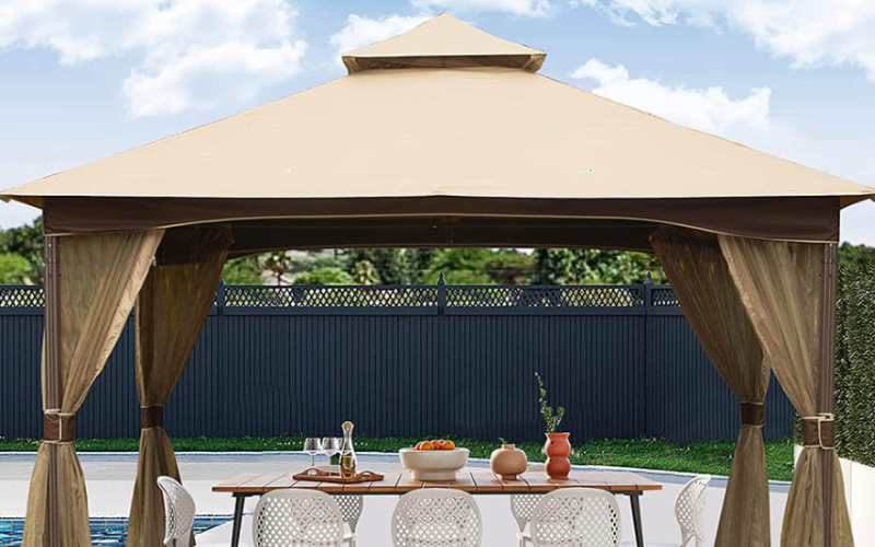 A poolside gazebo with a beige canopy, covering a dining table set with food and drinks, offering a shaded area for outdoor dining.
